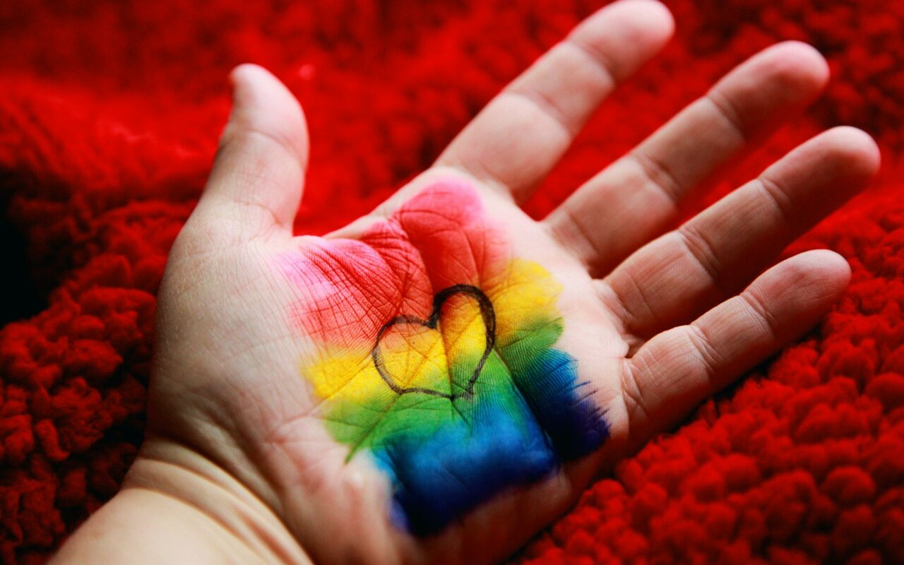 Un cuore formato da fili colorati arcobaleno appoggiato sul palmo di una mano